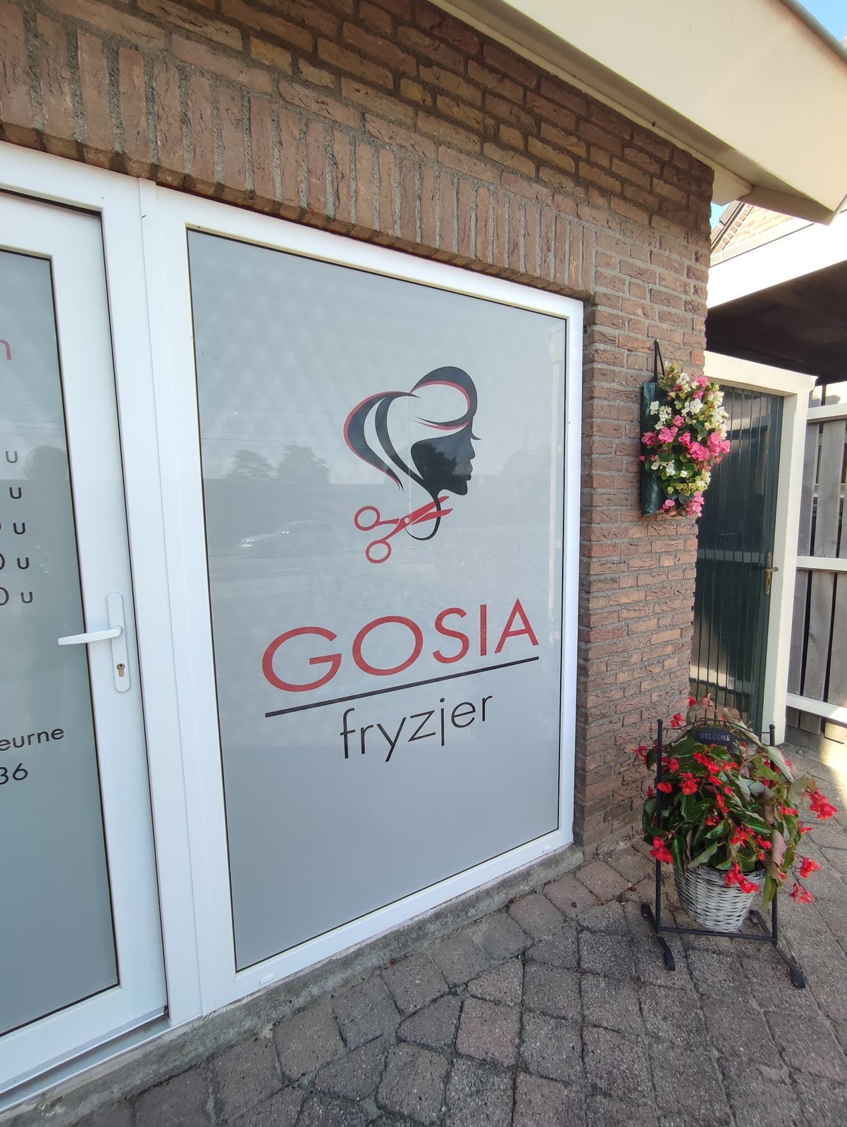 De gevel met het raam waarop GOSIA fryzjer staat en bloembakken bij de deur