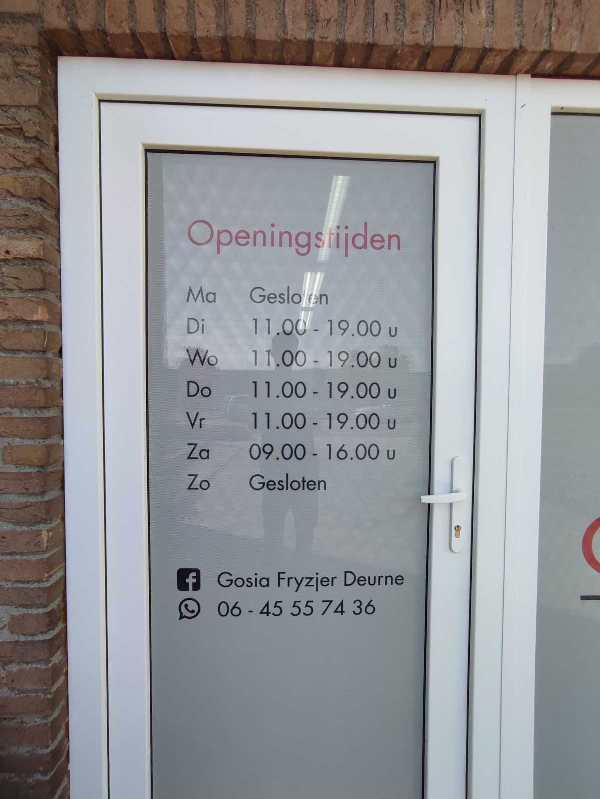 De deur van de salon met de openingstijden en het WhatsApp-nummer erop